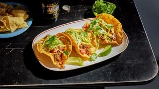 Puffy Tacos filled with ground beef shredded lettuce and pico de gallo with lime wedges and beer.