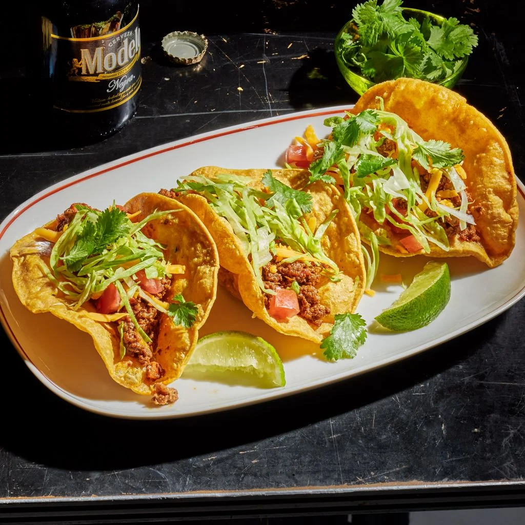 Puffy Tacos filled with ground beef shredded lettuce and pico de gallo with lime wedges and beer.