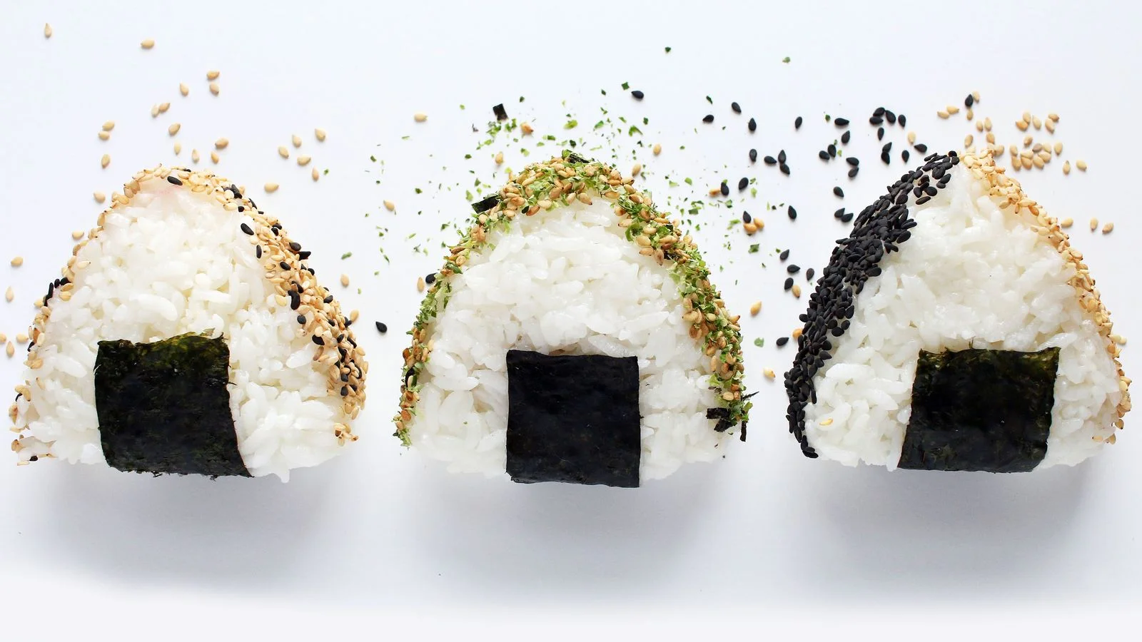 Three triangle onigiri with various furikake or sesame seed toppings.