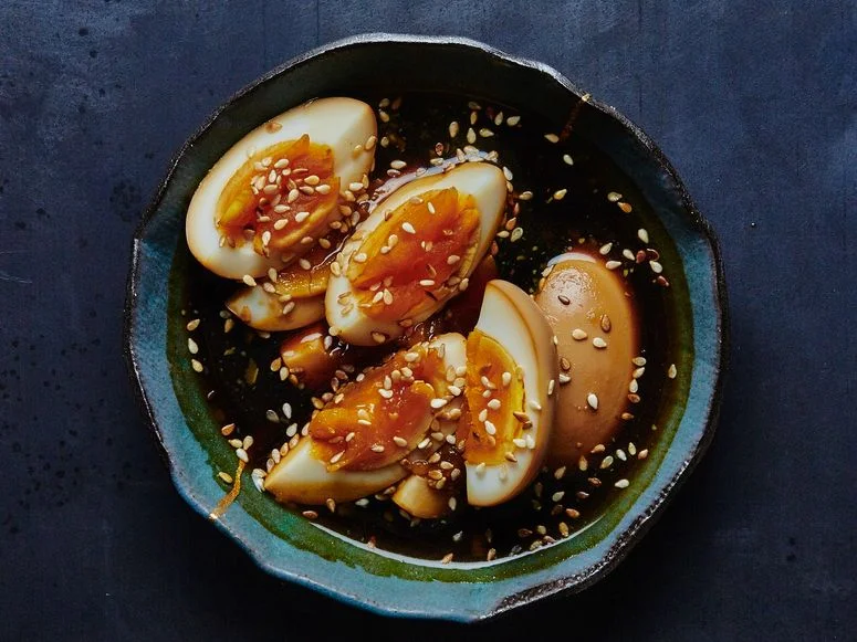 A bowl of quartered marinated eggs sitting in their soybased pickling liquid topped with sesame seeds.