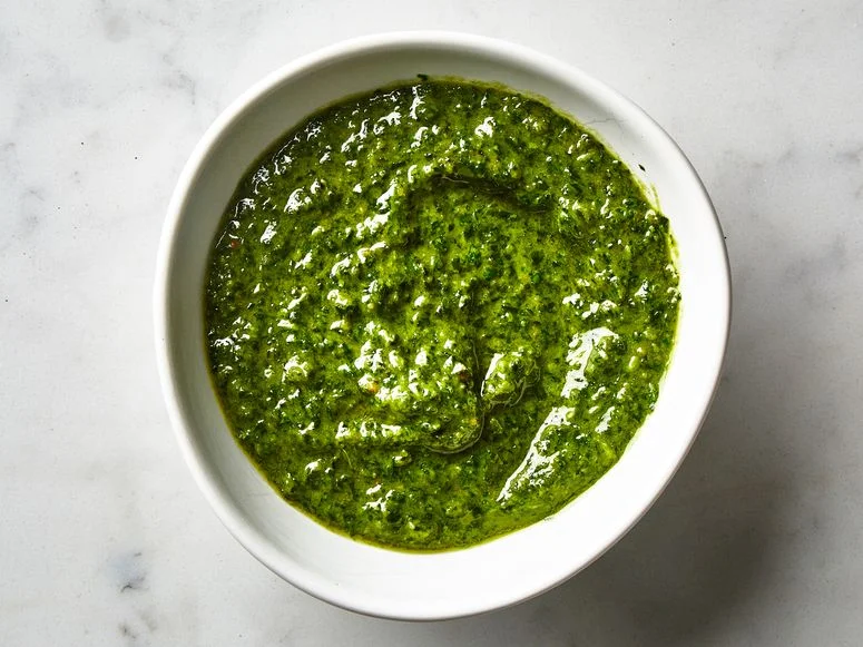 A white bowl on a marble counter filled with bright green basil pesto thick enough to hold a swirl.