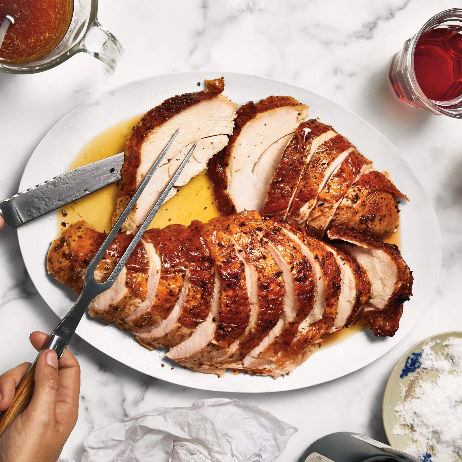 Two sliced turkey breasts on a platter being served with a carving fork and knife.