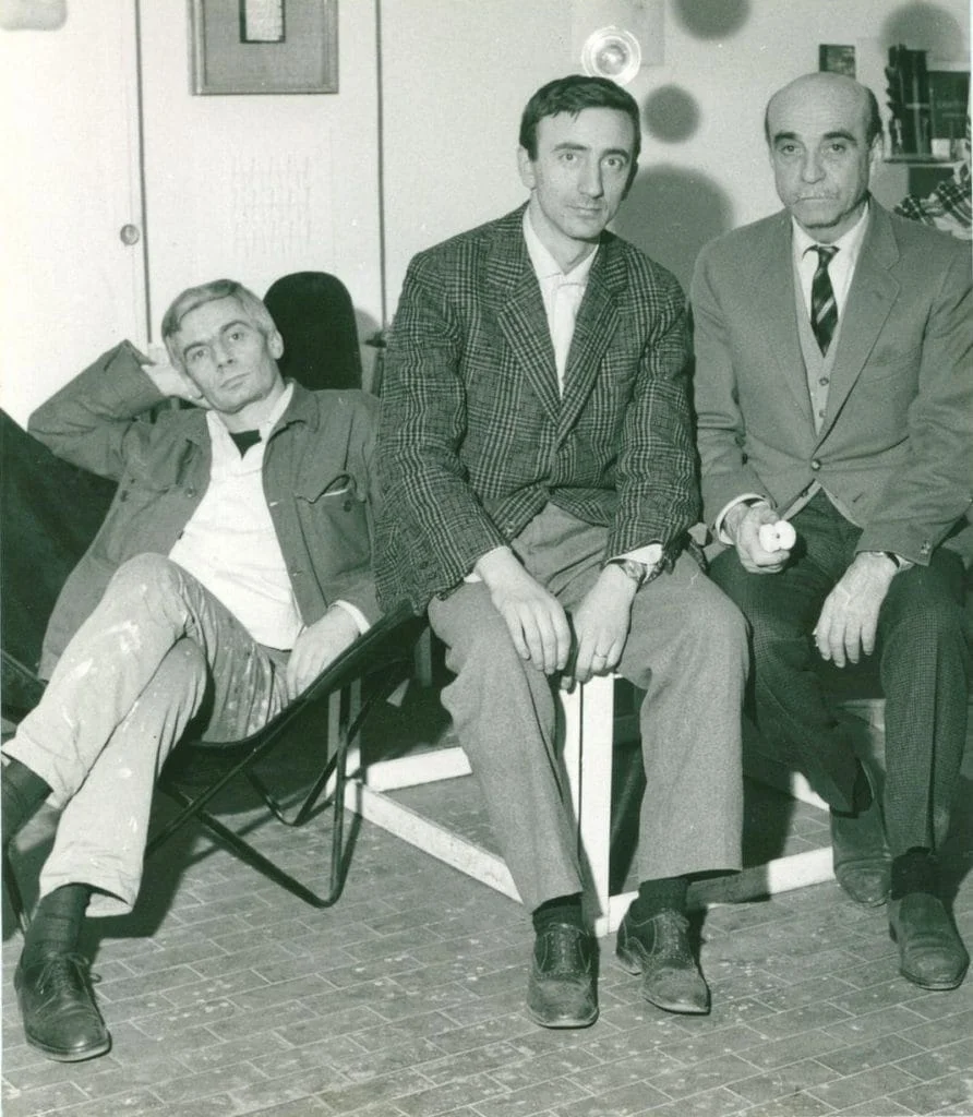 Black and white photograph of artists Enrico Castellani, Agostino Bonalumi, and Lucio Fontana seated together, circa 1960s. Courtesy Archivio Bonalumi.