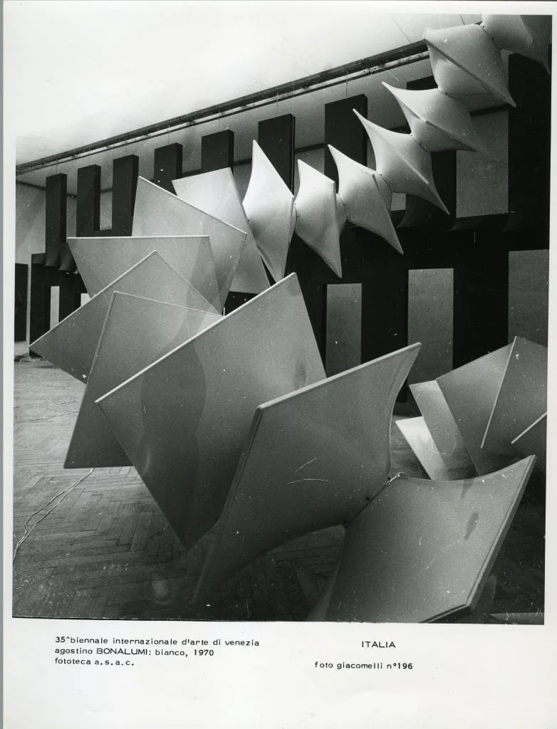 Agostino Bonalumi, 'Struttura modulare bianca,' 1970, installation view at the 35th Venice Biennale, Italian Pavilion, 1970. Black and white photograph showing the large-scale modular white sculpture filling the exhibition hall, its repeating angular geometric forms cascading across the floor and suspended toward the ceiling against a backdrop of dark rectangular wall elements. Photo Giacomelli no. 196. Archivio Storico della Biennale di Venezia / Archivio Storico delle Arti Contemporanee.