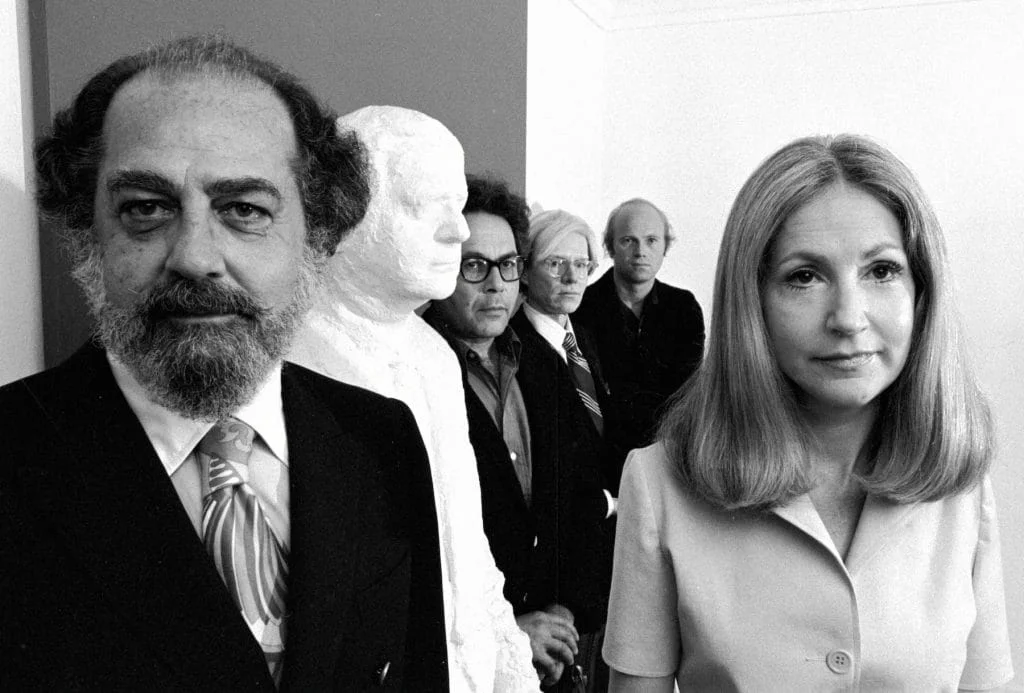 Black and white photo of four people standing near a white sculptural bust in what appears to be an art gallery or museum setting