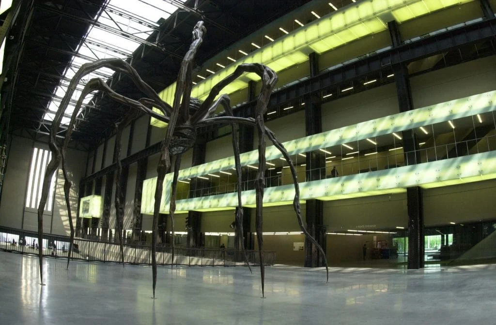 Towering bronze spider sculptures by Louise Bourgeois installed in the vast Turbine Hall of Tate Modern, London, dwarfing visitors below