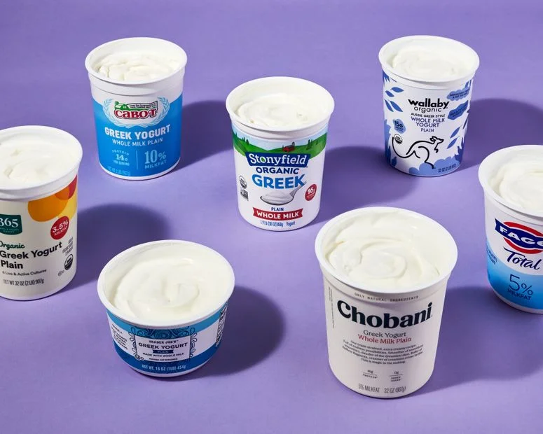 Seven containers of open greek yogurt on purple background.