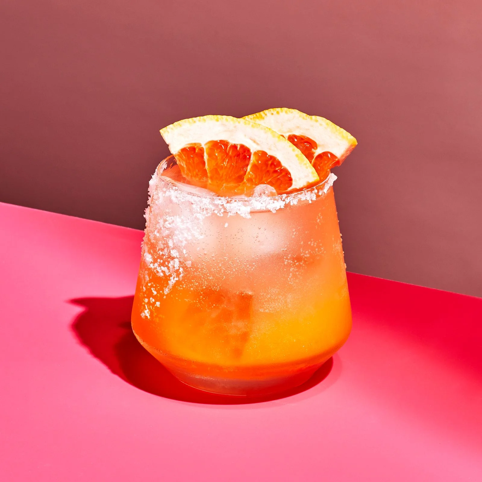 A saltrimmed paloma cocktail served over ice and garnished with grapefruit wedges.