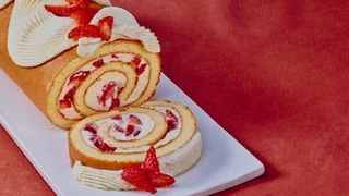 Sliced strawberry Swiss roll cake filled with whipped cream and fresh strawberries on a white platter.