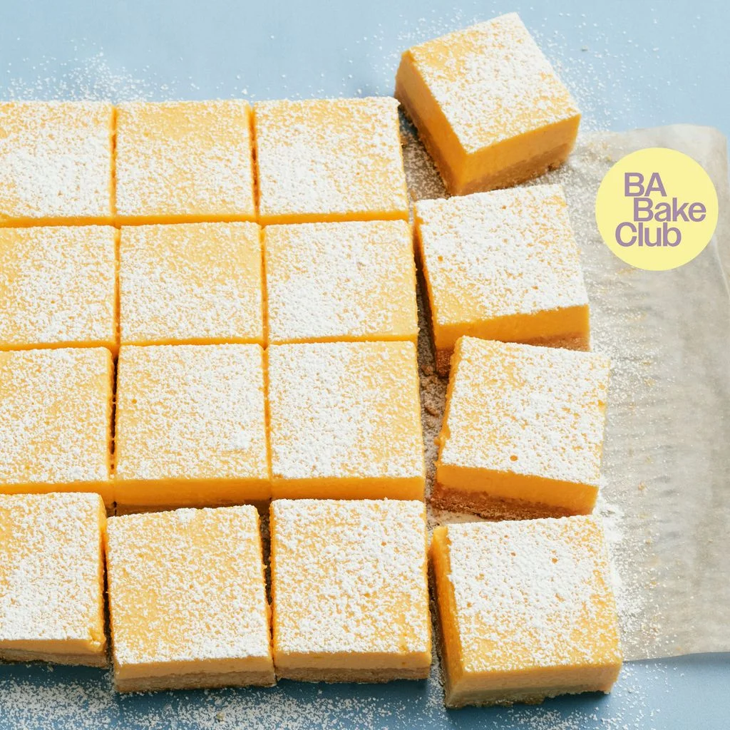 Lemon bars dusted with confectioner's sugar cut into squares on a piece of parchment paper.