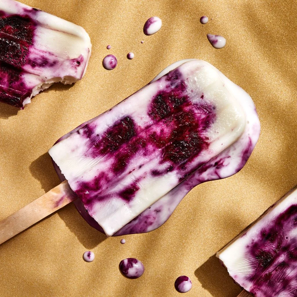 Slightly melted Yogurt​Berry Paletas on a beige background