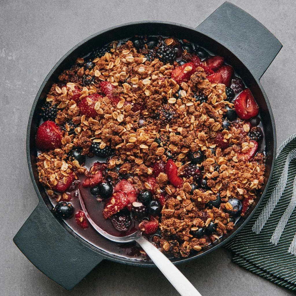 Macerated strawberries blueberries and blackberries in a cast iron skillet topped with streusel.