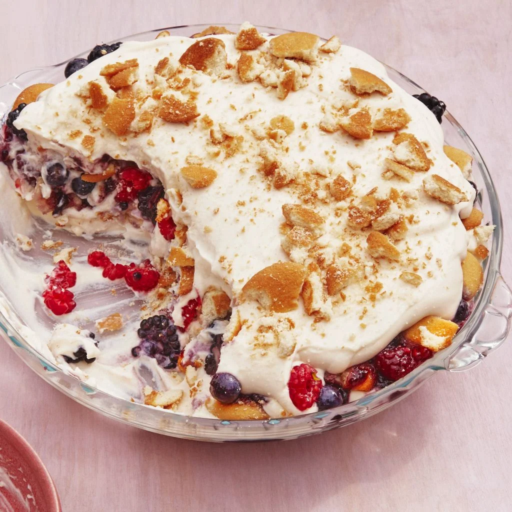 Layered berry pudding topped with whipped cream and crushed vanilla wafers in a glass serving dish.