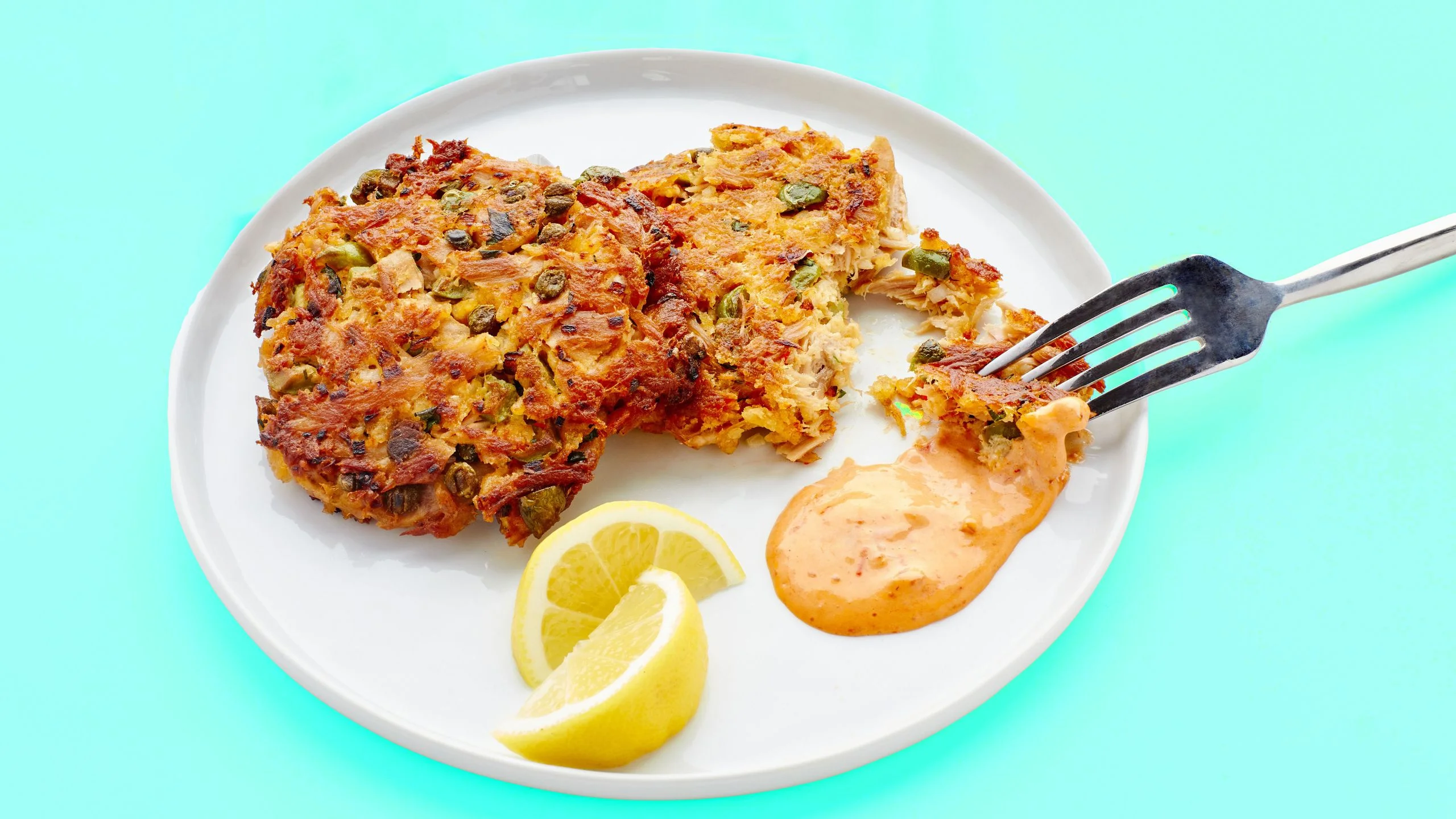 Crispy homemade tuna patties served on a white plate with spicy mayo dipping sauce and lemon wedges
