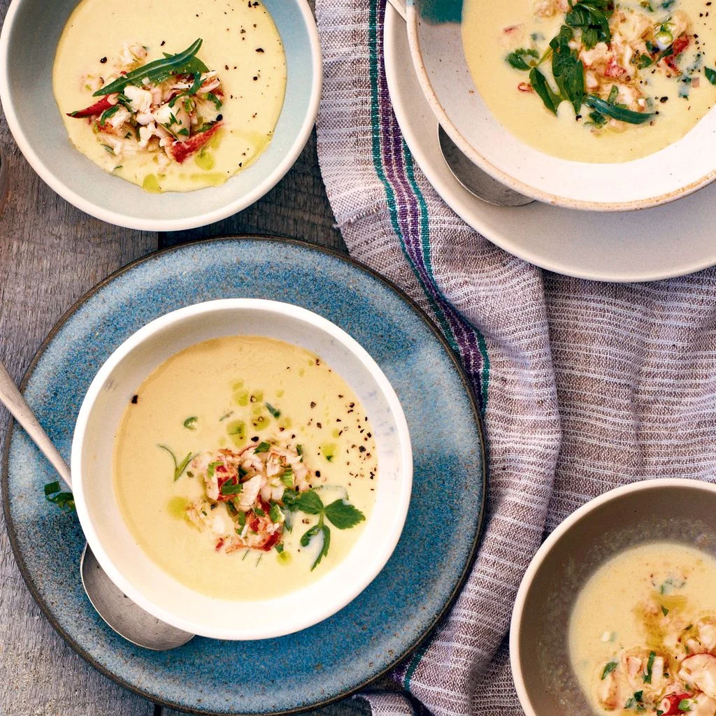 Several bowls of creamy corn soup topped with lobster and chopped herbs.