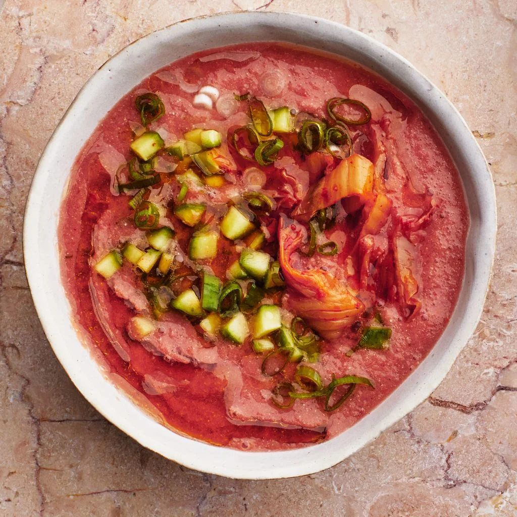 Bowl of kimchimelon gazpacho topped with chopped kimchi diced cucumber scallions and olive oil.