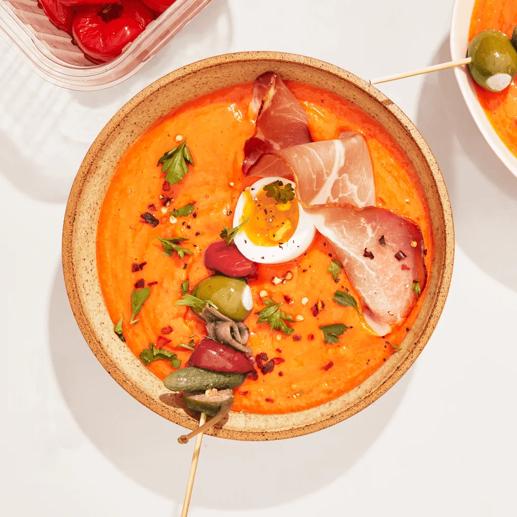 saucy bright orange red dish with skewer and jammy egg in a tan plate on white surface and accompanying dish on the side
