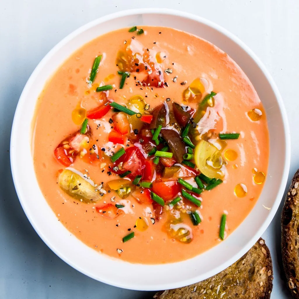 A bowl of gazpacho topped with chopped tomatoes and chives.