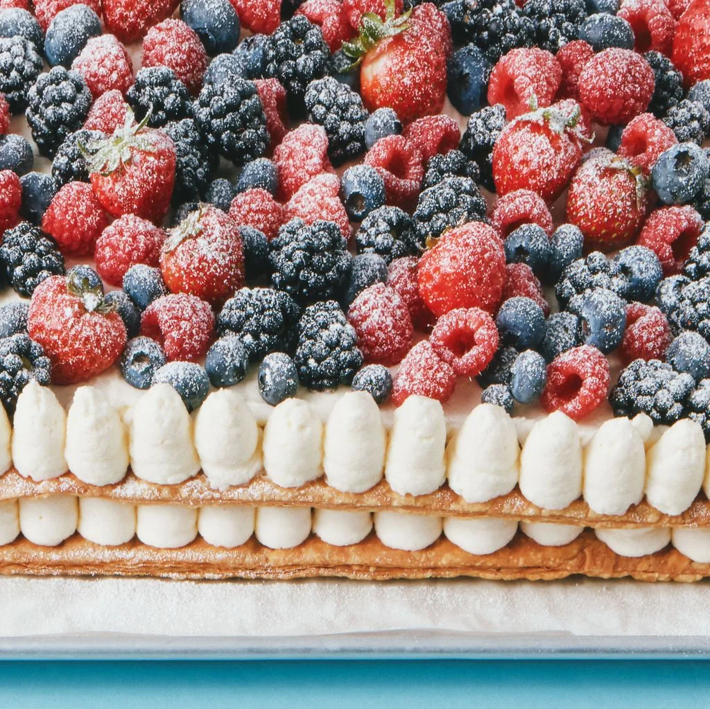 A berries and cream puff pastry on sheet pan against a blue background