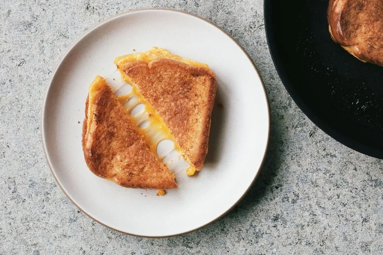A halved grilled cheese on a plate with melting cheese.
