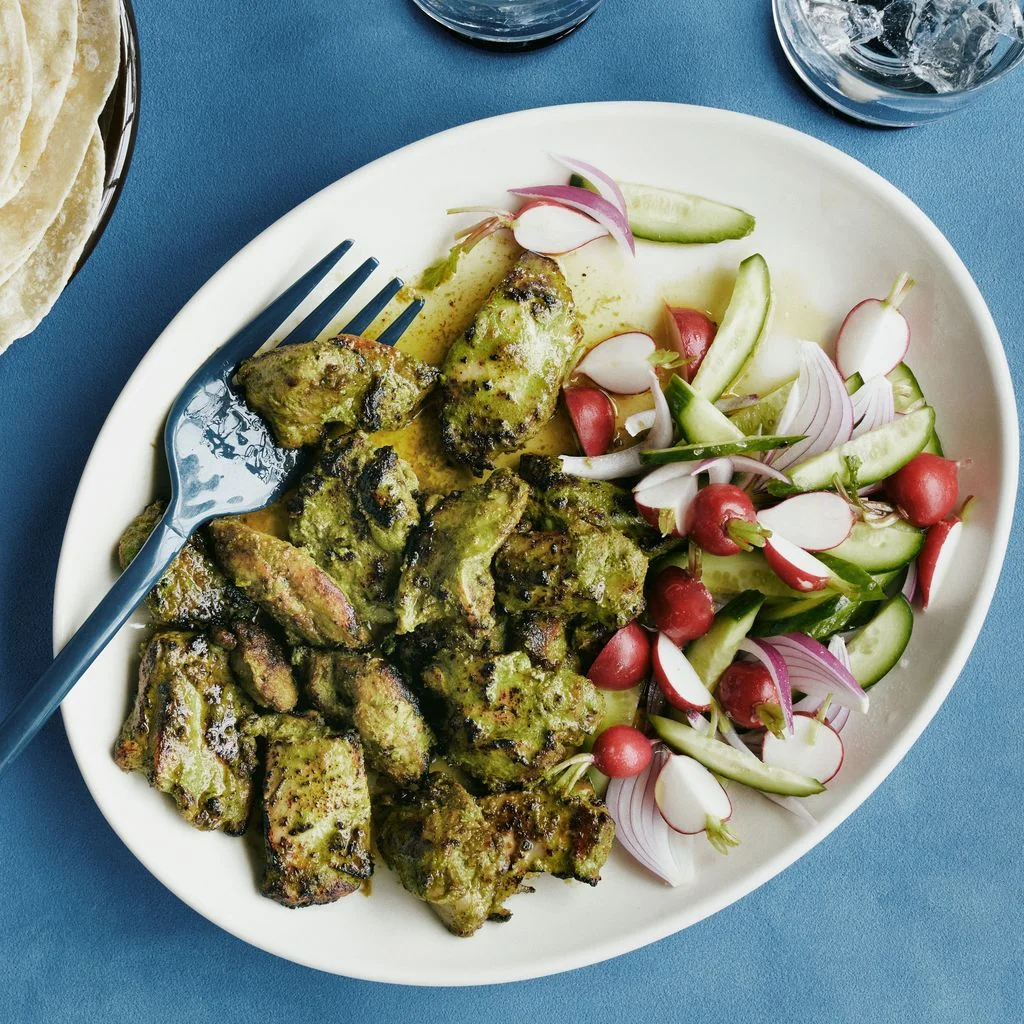 Boneless chicken thighs marinated in green chutney and broiled on a platter with red onions radishes and sliced...
