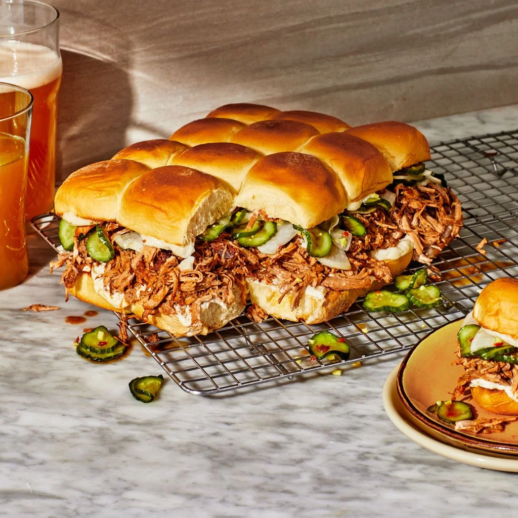 Pork Adobo Sliders with lots of pickles spilling out on a marbled surface