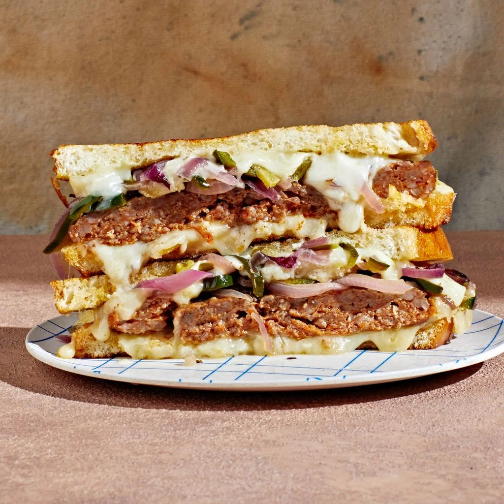Stacked halves of a chorizo patty melt with melted cheese and pickled onions on a plate