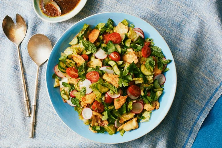 A large serving bowl of fattoush with shards of toasted pita cherry tomatoes cucumbers sliced radishes romaine and herbs...