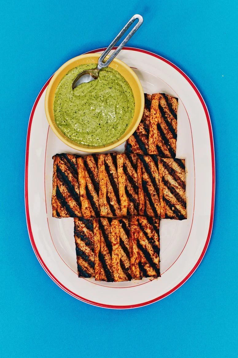tofu on a white plate with a bowl of sauce on the left side