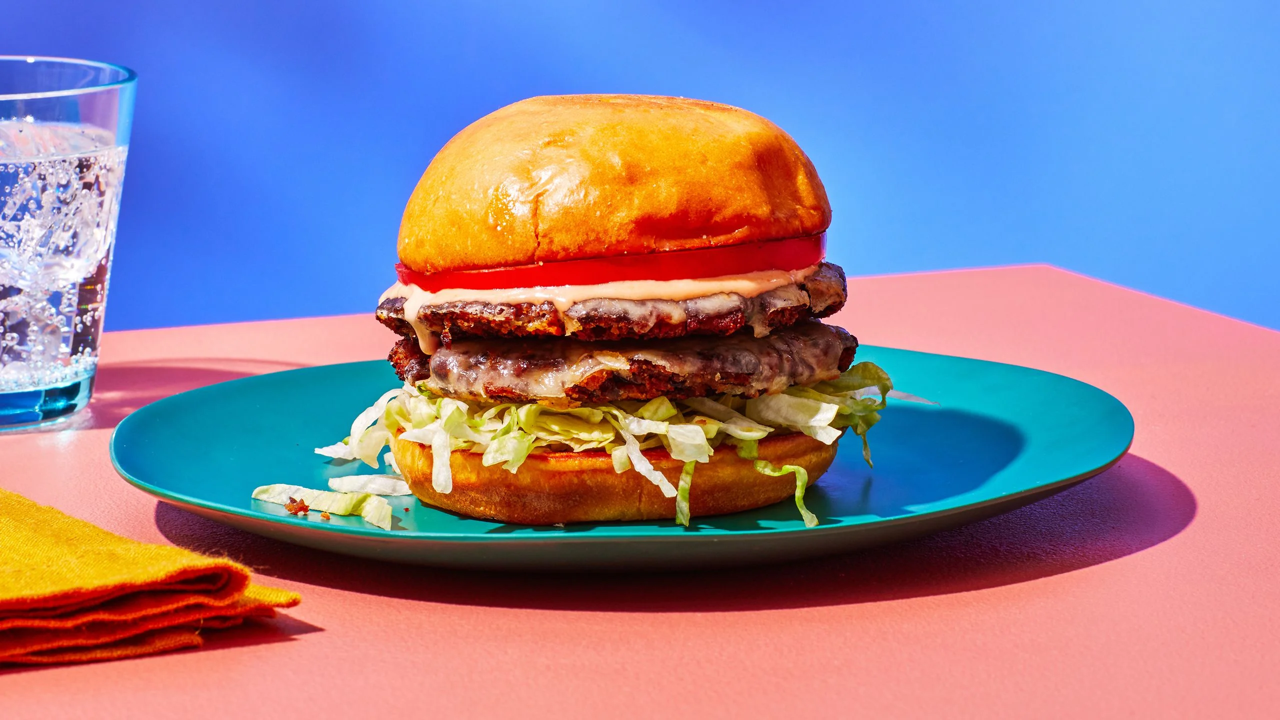 Side view of a black bean burger with two thin patties layered with shredded lettuce tomato and special sauce on a plate...