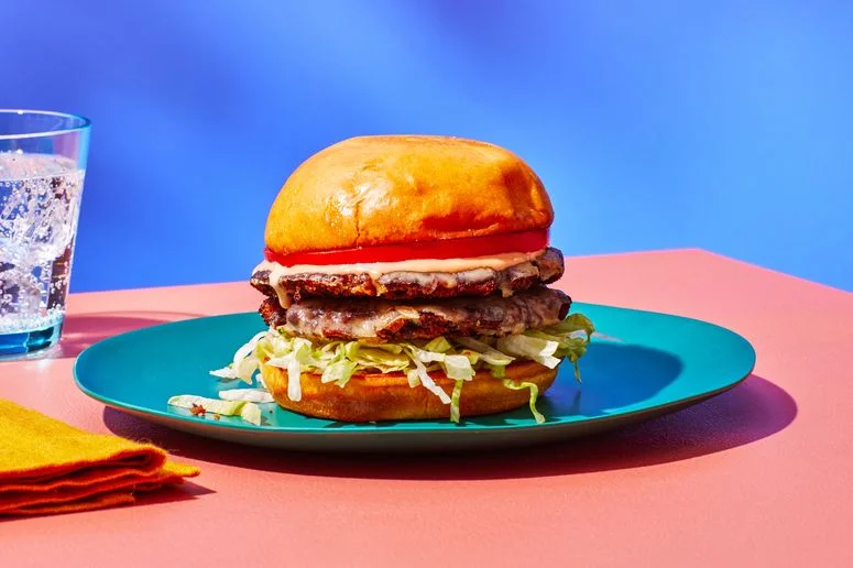 Side view of a black bean burger with two thin patties layered with shredded lettuce tomato and special sauce on a plate...
