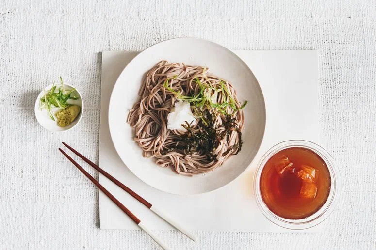 Soba noodles in a bowl with grated daikon thinly sliced scallions and shredded nori and served with wasabi and mentsuyu...