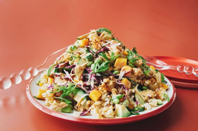 A pile of crispy rice diced mango shredded purple cabbage julienned radishes sliced Persian cucumbers sliced avocado...