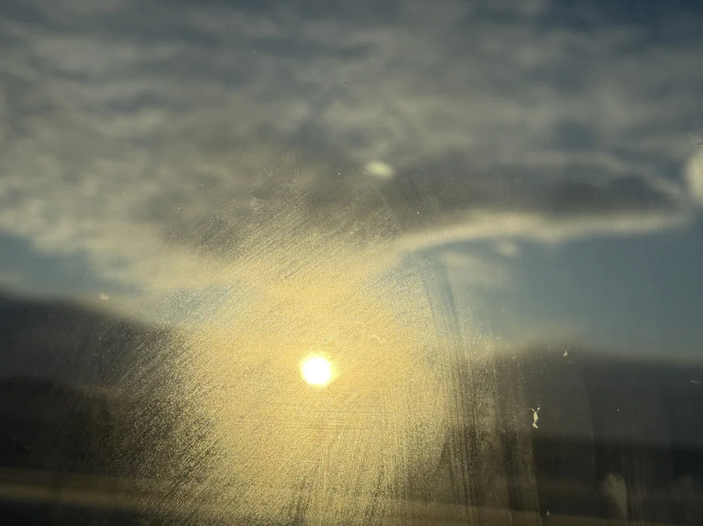 An iPhone photograph featuring a blurry image of the setting sun as seen through a dirty window